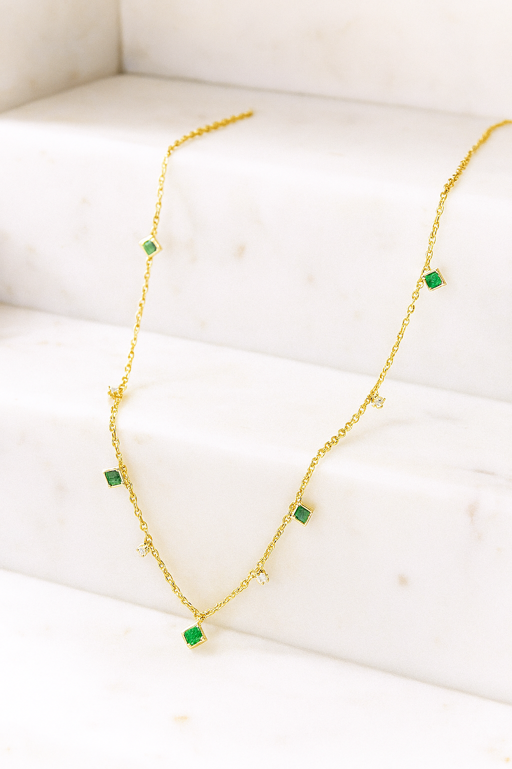 Gold necklace with green gemstones on a white surface