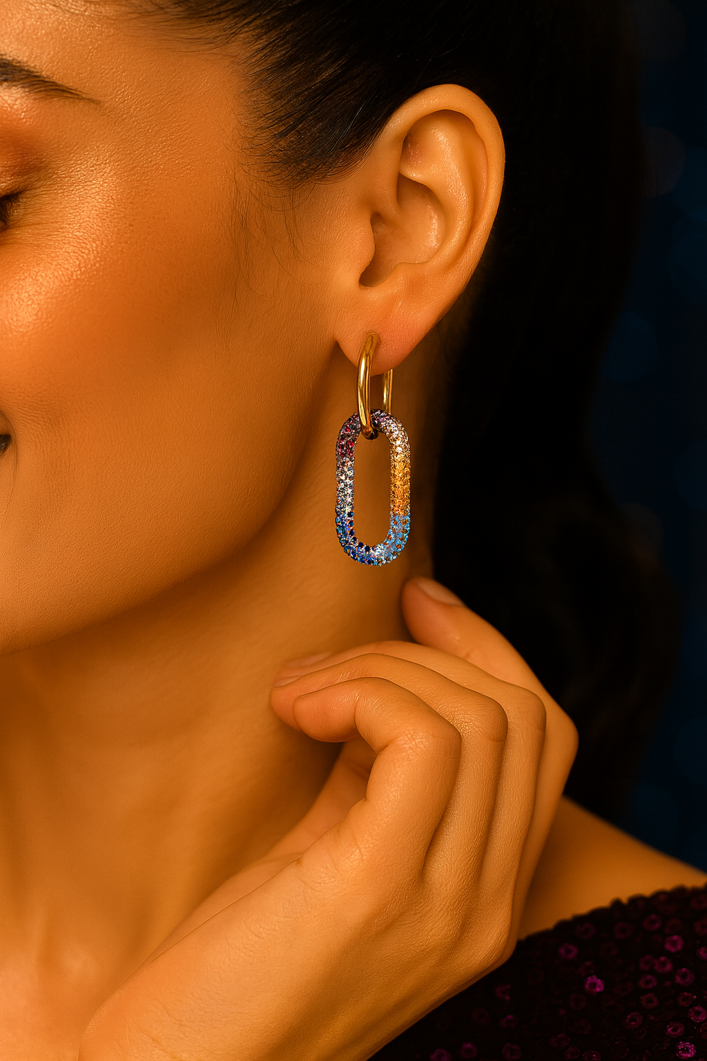 Gold hoop earrings with multicolored gemstones on a glittery background